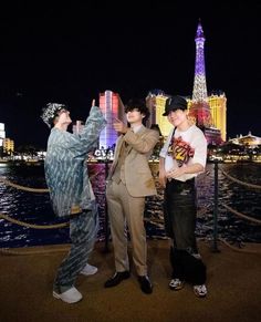 three men standing next to each other in front of the eiffel tower at night