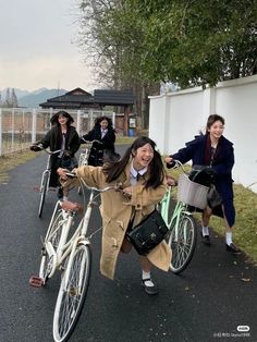 three women riding bikes down a street next to a white fence