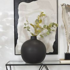 a black vase sitting on top of a glass table next to a metal sculpture and art