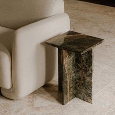 a marble side table sitting next to a white chair on a carpeted room floor