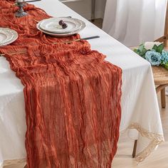 the table is set with two plates and an orange cloth draped over it, along with other place settings