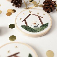 two embroidered christmas ornaments on a table with confetti, pine cones and decorations