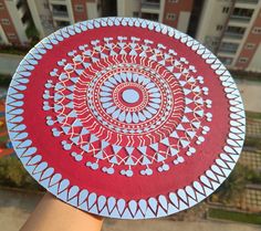 a hand holding a red and white plate with an intricate design on the bottom, in front of a building