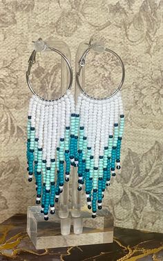 two pairs of beaded hoop earrings on a stand with a wallpaper behind it