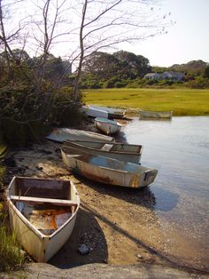 there are several small boats sitting on the shore by the water's edge, and one is empty