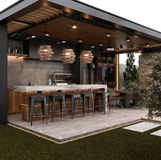 an outdoor kitchen with bar stools and lights on the ceiling is surrounded by grass