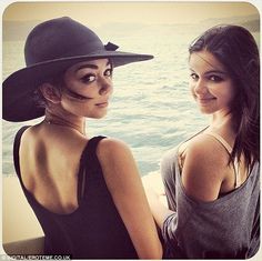 two young women are posing for a photo together in front of the ocean, one is wearing a black hat and the other wears a gray tank top