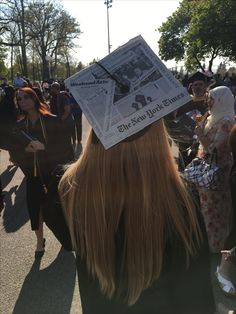 a woman with a newspaper on her head walking down the street in front of a crowd