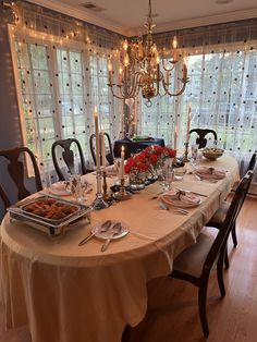 a dining room table is set with plates, silverware and candles in front of the window