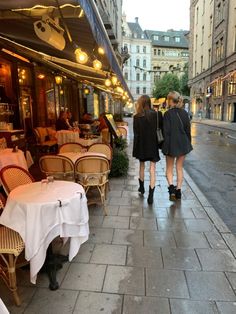 two women walking down the street in front of tables and chairs