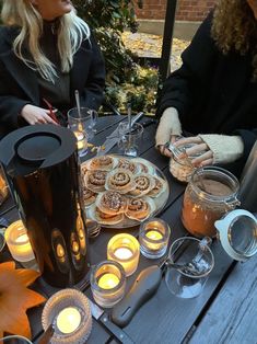 two women sitting at an outdoor table with food and candles in front of their faces