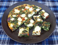 a pizza with spinach, cheese and other toppings cut into squares on a black plate