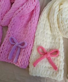 two knitted hats with pink bows on the top and one white hat with pink bow