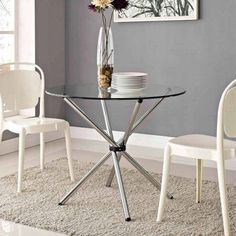 a glass table with two white chairs and a vase filled with flowers on top of it