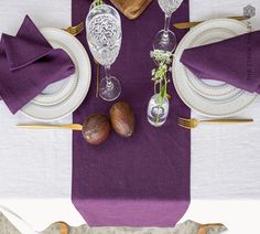 the table is set with silverware and purple napkins