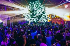 a large group of people standing in front of a christmas tree with lights on it