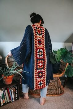 a woman standing in front of a plant wearing a blue crocheted cardigan