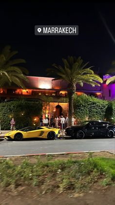 two cars parked in front of a building with palm trees and people standing outside it