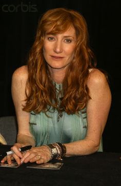 a woman sitting at a table in front of a black backdrop with her hand on the book