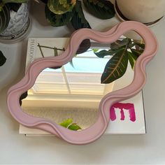 a pink mirror sitting on top of a table next to a vase with flowers in it