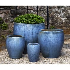 three blue vases sitting next to each other in front of a stone wall and planter