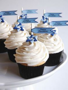 cupcakes with white frosting and blue decorations on a cake platter, labeled happy hanukkah