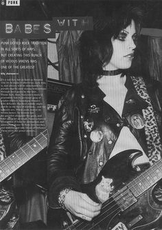 a woman holding a guitar in her right hand and wearing a leather jacket with leopard print on it