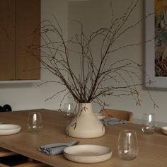 there is a vase with some branches in it on the table next to wine glasses