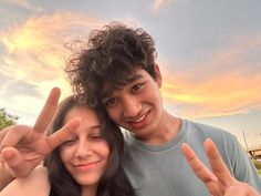 a man and woman are making the peace sign with their hands as the sun sets in the background