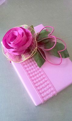 a pink gift box with a rose on the top and green leaves attached to it