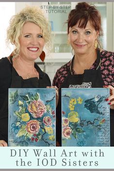 two women standing next to each other holding paintings