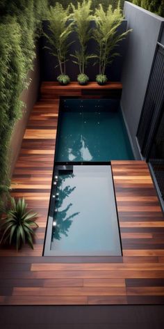 an outdoor pool with wooden decking and plants on the side, surrounded by greenery