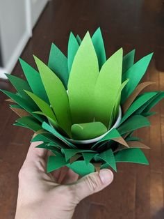 a hand holding a paper flower on top of a wooden floor