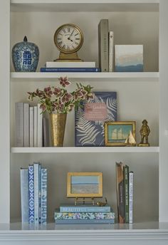 a shelf with books, flowers and a clock on it's top is shown