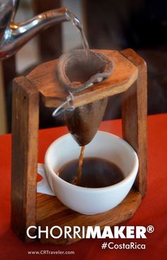 a coffee maker pours water into a cup on top of a wooden stand with a red table cloth