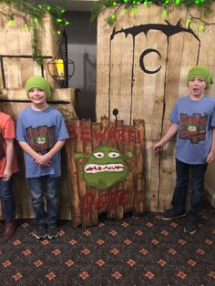 three young boys standing next to each other in front of a wooden sign with an angry grin face on it