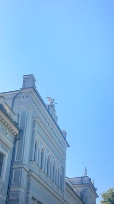 a clock on the side of a building with trees in the foreground and blue sky behind it