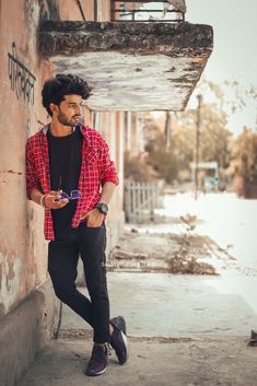 a man leaning against a wall with his hand on his hip and looking at the camera