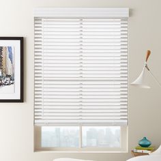 a window with white blinds in the corner next to a lamp and pictures on the wall