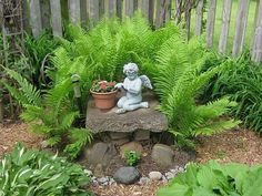 a small statue sitting on top of a rock surrounded by plants