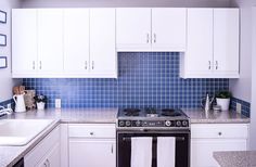 a kitchen with white cabinets and blue tile backsplash, black stove top oven