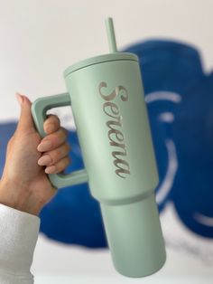 a person holding a green coffee cup with the word serendow on it in front of a blue and white background