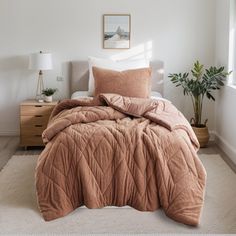 a bed in a bedroom with an orange comforter and pillows on it, along with a potted plant