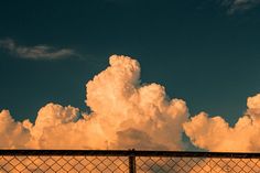 an airplane is flying in the sky behind a chain link fence with clouds above it