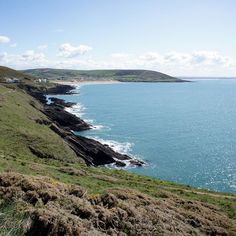 a grassy hill next to the ocean on a sunny day