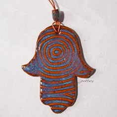 a ceramic hamsa hanging from a cord on a white surface with an orange and blue swirl design