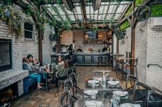 people sitting at tables in a restaurant with plants growing on the walls and windows above them