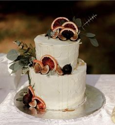 a three tiered cake with figs and greenery on the top is decorated with fresh fruit