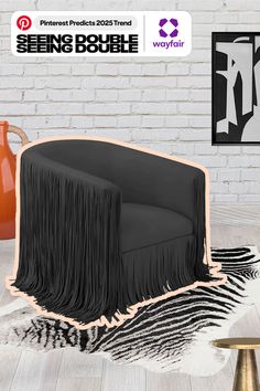 a black chair with fringe on it in front of a white brick wall and an orange vase