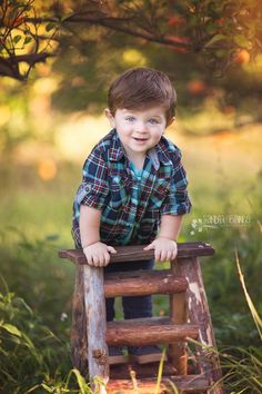 a little boy standing on top of a wooden ladder in the grass with trees behind him